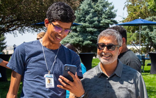 A male student apprentice showing his phone to a Micron employee